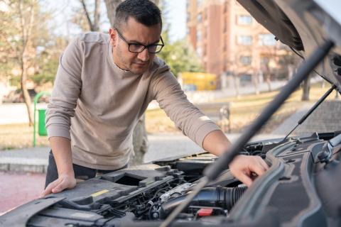 Man leaning over and looking under car hood.